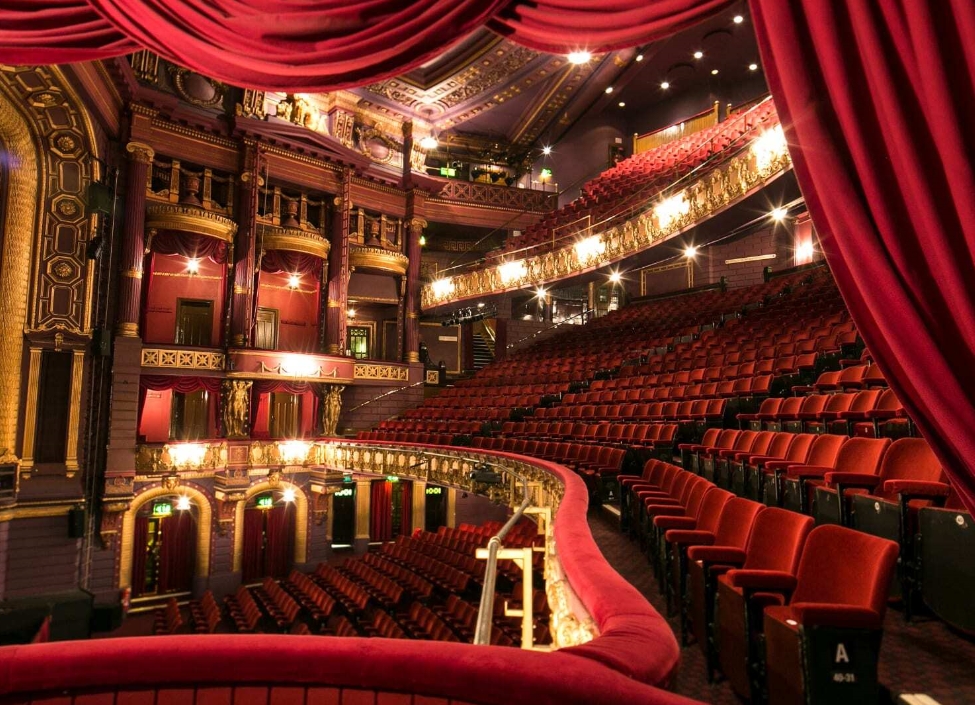 The inside of the Manchester Palace Theatre & Opera House, with a stage surrounded by red seats and numerous balconies